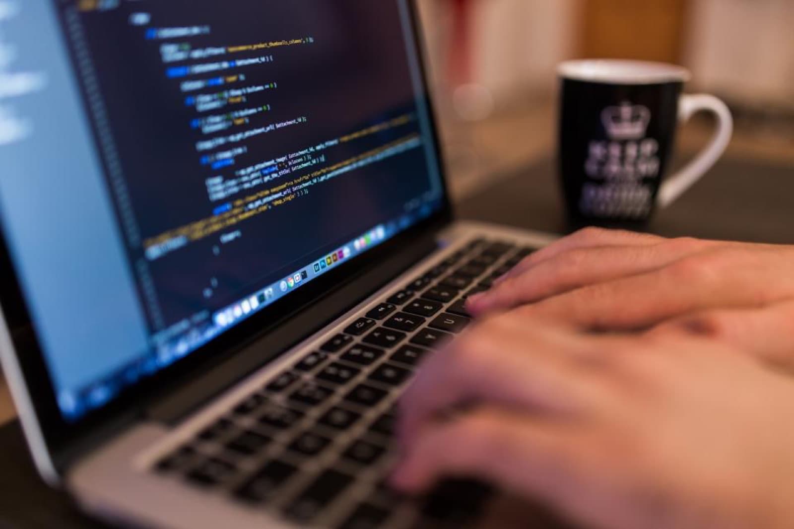 Code on a laptop screen beside a coffee mug
